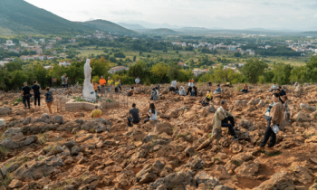 Pilgrims praying on Apparition Hill in Medjugorje overlooking the valley